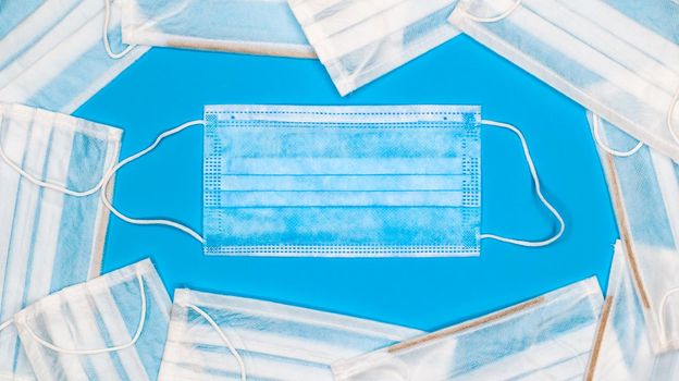 Coronavirus protection. Many antiviral protective medical face masks with ear loops spread out on a blue background. Surgical mask background. Respiratory syndrome, coronavirus disease COVID-19