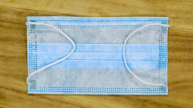 One 3-ply disposable surgical face mask with rubber pads covering the mouth and nose on a wooden table. The concept of protection from bacteria, healthcare and medicine. COVID-19. Dangerous virus