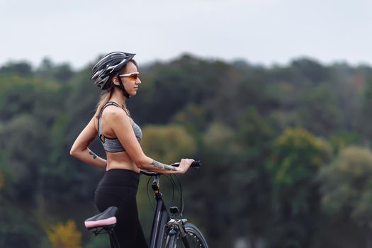 Fit young woman wearing sportswear standing with her bicycle on rocky background at autumn day