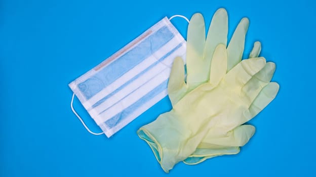 A pair of disposable latex medical gloves and a surgical mask on a blue background. Covid-19 virus protection concept. Protective items. Means of protection