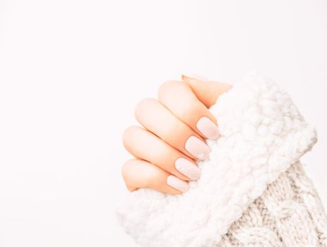 Female hand with professional manicure of natural pastel color and art design wearing in wool sweater.