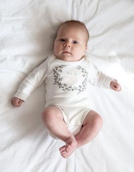 Portrait of a newborn baby girl who lies on a bed. Three-month-old girl in white suit lies on a veil view from above. High quality photo