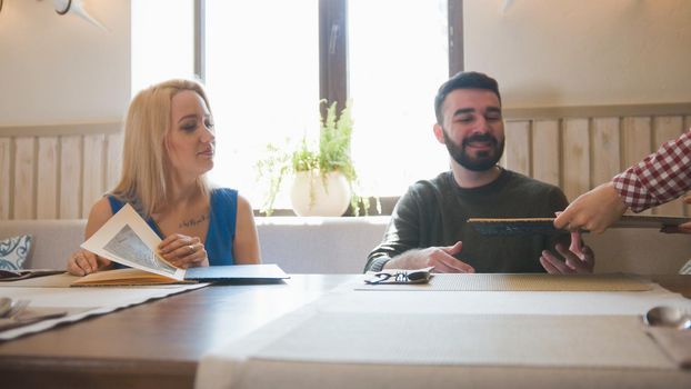 Waiter in cafe shows menu for young couple, close up