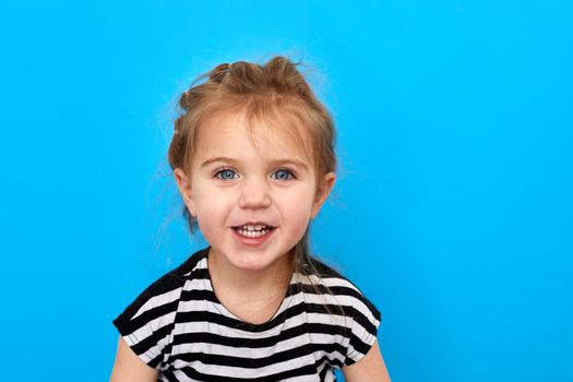 Close-up studio shot of a lovely little girl in t-shirt posing against a blue background. Looks at the camera and smiles