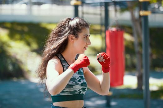 Attractive young woman standing in a position of boxer, workout in summer park, horizontal