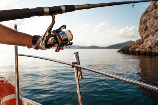 Close up photo of male hands holding fishing rod while fishing on sailboat in open sea