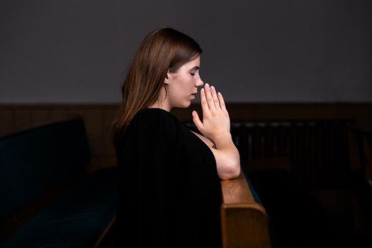 A Christian girl in white shirt is sitting and praying with humble heart in the church.