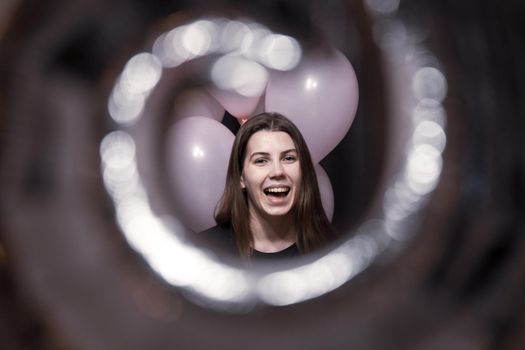 View through the tunnel. The face of a pretty girl with an emotion of joy that holds pink balloons on her birthday
