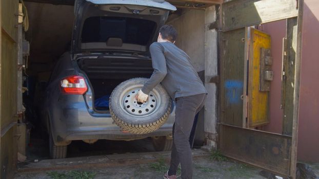 Young man puts a wheel in car trunk in the garage, close up