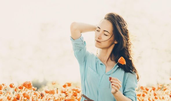 Outdoor portrait of pretty romantic young woman with poppy in spring. Brunette female with dreamy emotions relaxing in flower meadow.