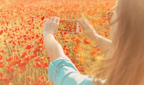 Young woman taking a photo with smartphone of red poppies flower meadow in summer outdoor.