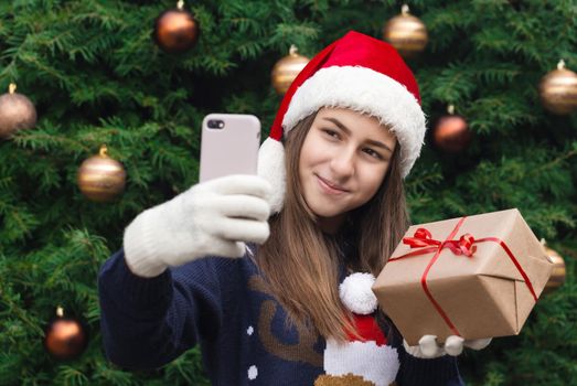 Christmas online greetings. girl in santa claus hat talks and using mobile smartphone for video call friends and parents. Christmas during coronavirus.