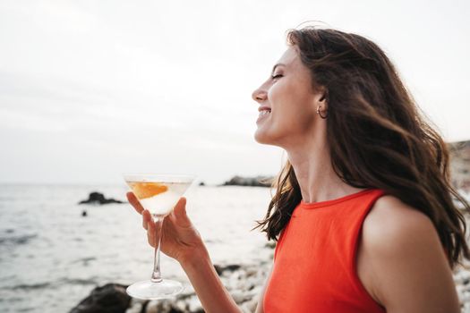 Portrait of young woman with cocktail glass chilling on a beach, close up