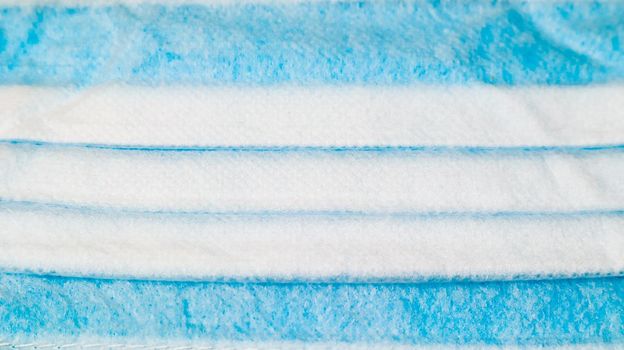 One 3-ply disposable surgical face mask close-up with rubber pads covering mouth and nose against blue background. The concept of protection from bacteria, healthcare and medicine. COVID-19