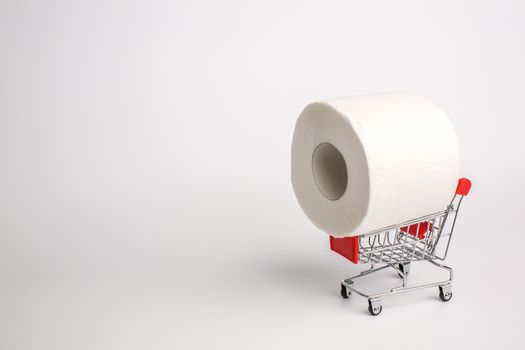 Toilet paper in toy shopping cart, stockpiling concept due to coronavirus outbreak. Panic purchase of toilet paper during quarantine.