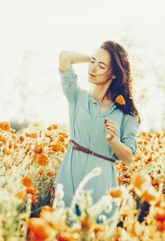 Attractive brunette young woman with dreamy emotions relaxing in poppies summer meadow.