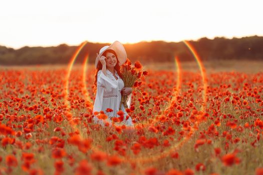 Beautiful smiling happy redhead woman in white hat on green field with bouquet of poppies in summer sunset