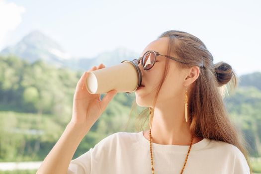 Beautiful young woman drinking coffee in summer morning on background of mountains.