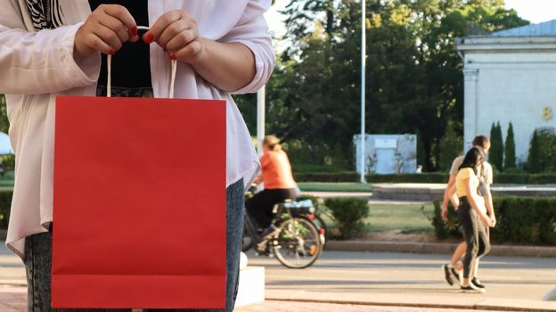 Close-up of a shopaholic woman with a red paper shopping bag in her hands. Crop the photo. Consumerism, shopping, lifestyle concept. Copy space for your logo. Black Friday.