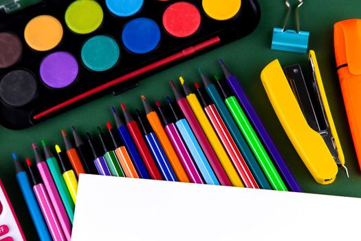 School office supplies stationery on a green background desk with white paper above copy space. Back to school concept