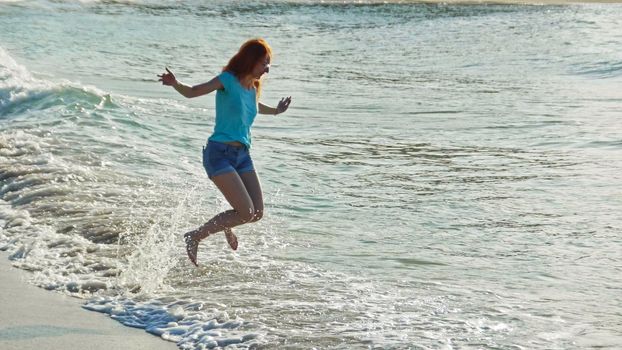 Young woman with long red hair play with waves running, feeling the sea, seascape beach of Dominican Republic, Caribbean sea