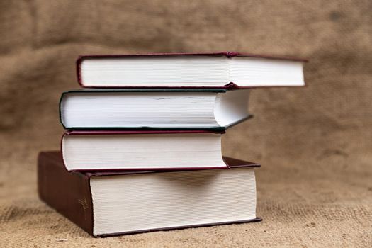 A stack or bound of old books lies on a burlap texture with place for tex