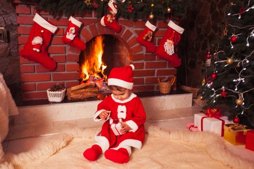 Little girl sitting near fireplace and christmas tree with gift boxes