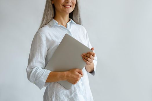 Smiling middle aged lady wearing elegant blouse holds modern laptop on light grey background in studio closeup, space for text