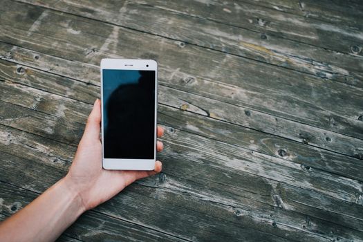 Female hand with mobile phone on wooden background, point of view.