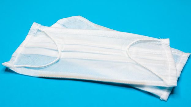 Two three-layer disposable surgical face masks with rubber pads to cover the mouth and nose against a blue background. The concept of protection from bacteria, healthcare and medicine. COVID-19