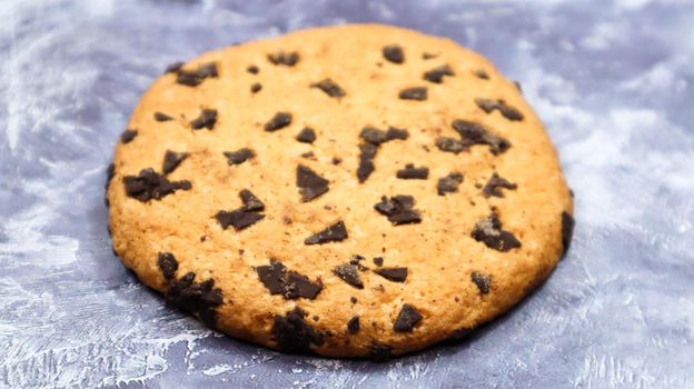 One soft, freshly baked chocolate chip cookie on a gray marble kitchen countertop. American traditional dessert. Delicious sweet food. Homemade baking concept for the holiday. Culinary background.