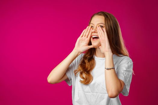 Young woman shout using her hand as a tube against pink background