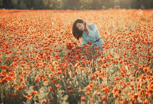 Romantic beautiful young woman walking in red poppy flower field in summer day.