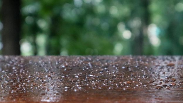 Empty wooden table top with raindrops on blur fresh green abstraction from the garden. For product display mounting. Empty wooden table with blurred green nature background.