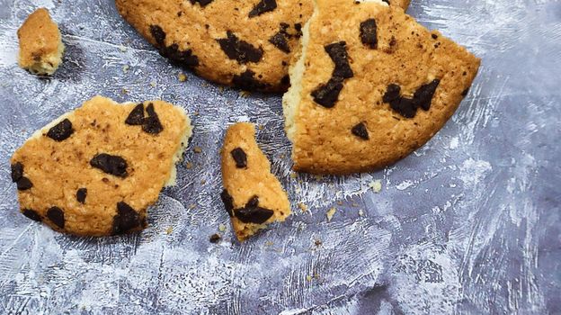 One soft freshly baked chocolate chip cookie with crumbs and chunks on a gray marble kitchen countertop. American traditional pastry, dessert. Delicious sweet food. Flat lay