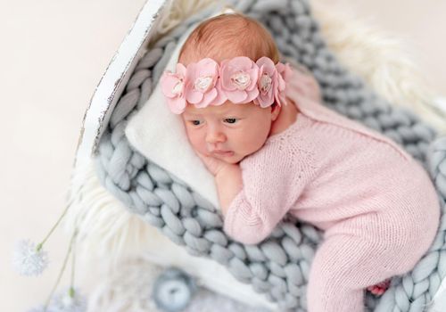 Charming newborn in floral diadem lying awake on tiny bed