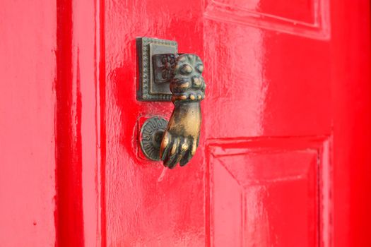 Red lacquered door with doorknocker Metal arm of woman