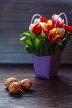 Easter beige eggs decorate with rope and bouquet of different color tulps on brown wooden background with copyspace