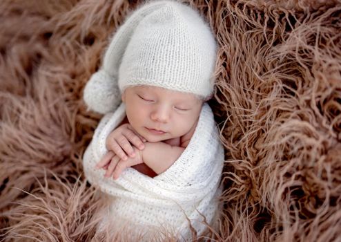 Cute sleeping newborn wearing white knitted hat