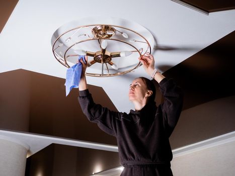 woman cleans the cobwebs and debris on the ceiling near the chandelier. Big house cleaning