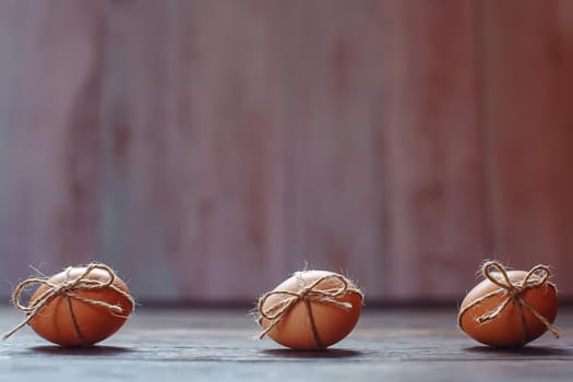 Easter beige eggs decorate with rope on brown wooden background with copyspace
