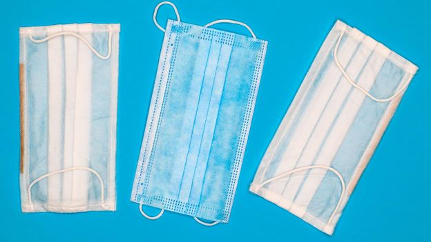 Three disposable surgical face masks with rubber pads to cover the mouth and nose on a blue background. The concept of protection from bacteria, healthcare and medicine. COVID-19. Dangerous virus.