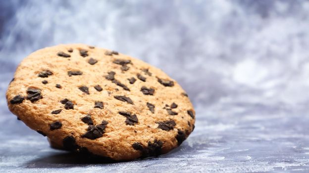 One soft, freshly baked chocolate chip cookie on a gray marble kitchen countertop. American traditional dessert. Delicious sweet food. Homemade baking concept for the holiday. Culinary background.