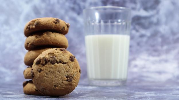 American chocolate chip cookies stacked on top of each other with milk in a glass on a gray background. Traditional rounded crunchy dough with chocolate chips. Bakery. Delicious dessert, pastries