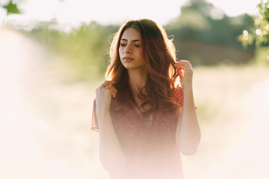 Portrait of beautiful young woman in with long brown hair in red pattern dress posing outdoors at summer sunset, dreaming, sensual, blurry white smoky background