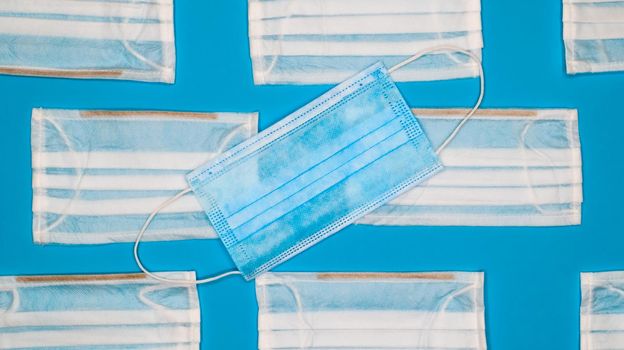Coronavirus protection. Many antiviral protective medical face masks with ear loops spread out on a blue background. Surgical mask background. Respiratory syndrome, coronavirus disease COVID-19