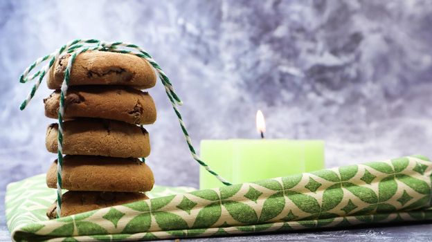 American chocolate chip cookies in a stack tied with thread on a green napkin and a candle. Traditional rounded crunchy dough with chocolate chips. Bakery. Delicious dessert, pastries