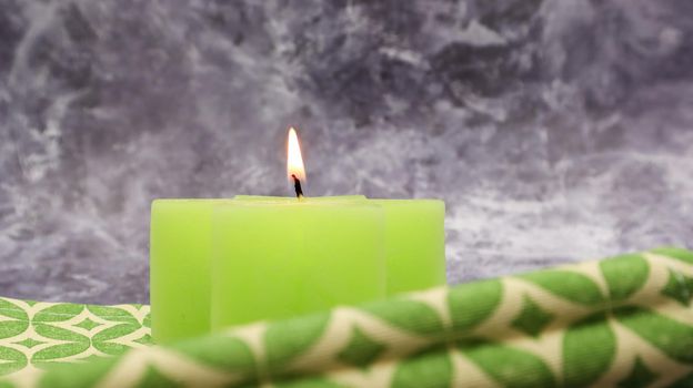 Composition with one green lit candle on a table with a green linen napkin against a beautiful gray marble background. Place for your text. Christmas decorations