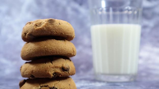 American chocolate chip cookies stacked on top of each other with milk in a glass on a gray background. Traditional rounded crunchy dough with chocolate chips. Bakery. Delicious dessert, pastries