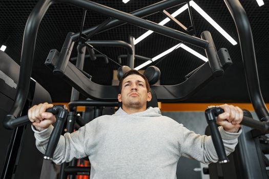 Young fit bodybuilder man doing arms workout training in the gym on machine, close up